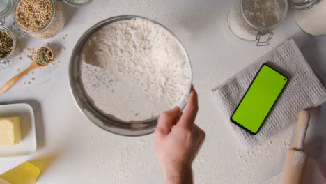 Fotografía-Cenital-De-La-Harina-Tamizada-En-La-Superficie-De-Trabajo-Para-Hornear-Con-Un-Teléfono-Móvil-De-Pantalla-Verde