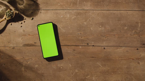 Fotografía-Cenital-De-Una-Persona-Recogiendo-Una-Hogaza-De-Pan-De-Una-Mesa-De-Madera-Con-Un-Teléfono-Móvil-De-Pantalla-Verde