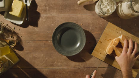 Fotografía-Cenital-De-Una-Persona-Cortando-Y-Untando-Una-Rebanada-De-Pan-Fresco-En-Una-Mesa-De-Madera