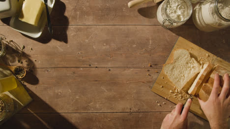 Overhead-Shot-Of-Person-Cutting-Slices-Of-Fresh-Bread-From-Loaf-On-Wooden-Table