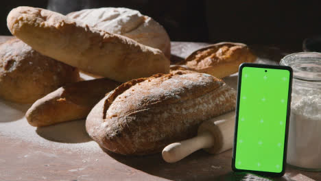 Zurückhaltender-Schuss-Von-Frisch-Gebackenen-Brotlaiben-Auf-Der-Arbeitsfläche-Mit-Greenscreen-Handy-1