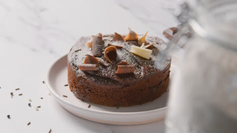 Homemade-Chocolate-Cake-On-Plate-On-Kitchen-Work-Surface-Behind-Ingredients