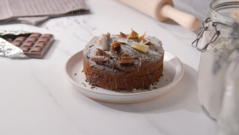 Homemade-Chocolate-Cake-On-Plate-On-Kitchen-Work-Surface-Dusted-With-Icing-Sugar-1