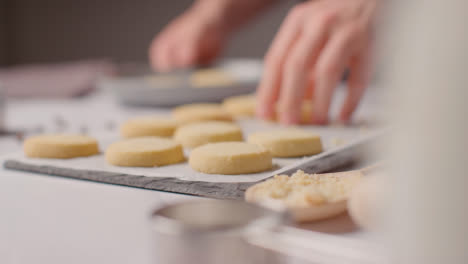 Person-Sprinkling-Sugar-Onto-Homemade-Shortbread-Cookies-On-Tray-On-Kitchen-Work-Surface