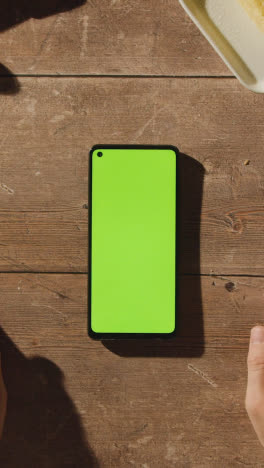 Vertical-Video-Overhead-Shot-Of-Person-Using-Green-Screen-Mobile-Phone-On-Wooden-Table