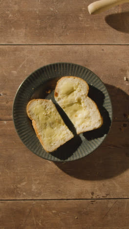 Vertical-Video-Overhead-Shot-Of-Person-Eating-Freshly-Baked-Bread-With-Butter-On-Wooden-Table-With-Hot-Drink