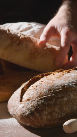 Vertical-Video-Low-Key-Shot-Of-Person-Picking-Up-Freshly-Baked-Loaf-Of-Bread-From-Work-Surface