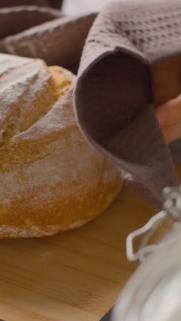 Vertical-Video-Shot-Of-Freshly-Baked-Loaf-Of-Bread-Being-Put-Down-Onto-Marble-Work-Surface