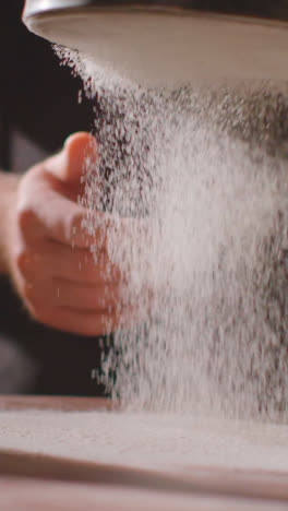 Vertical-Video-Overhead-Shot-Of-Flour-Being-Sieved-Onto-Work-Surface-For-Baking