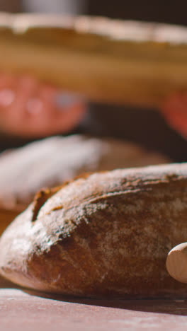 Vertical-Video-Low-Key-Shot-Of-Person-Putting-Freshly-Baked-Loaf-Of-Bread-Onto-Work-Surface