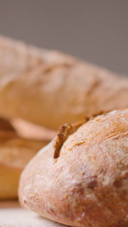 Vertical-Video-Shot-Of-Freshly-Baked-Loaves-Of-Bread-On-Work-Surface-With-Rolling-Pin