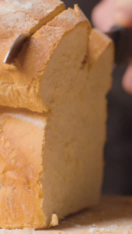 Vertical-Video-Close-Up-Of-Person-Cutting-Slices-Of-Fresh-Bread-From-Loaf