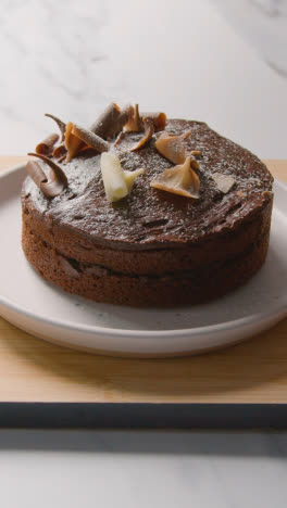 Vertical-Video-Of-Homemade-Chocolate-Cake-On-Plate-On-Kitchen-Work-Surface-Dusted-With-Icing-Sugar