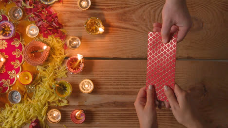 Overhead-Shot-Of-Person-Receiving-Gift-Of-Money-With-Burning-Lamps-Celebrating-Festival-Of-Diwali-1