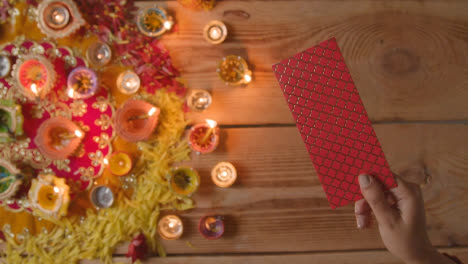 Overhead-Shot-Of-Person-Giving-Gift-Of-Money-With-Burning-Lamps-Celebrating-Festival-Of-Diwali