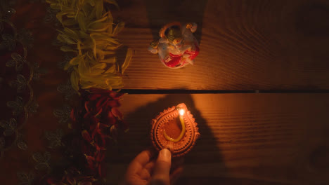 Mano-Poniendo-Lámpara-Diya-En-La-Mesa-Decorada-Para-El-Festival-De-Diwali-Con-Estatua-De-Ganesh