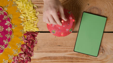 Clay-Pot-With-Lights-Being-Used-To-Celebrate-Indian-Wedding-Diwali-Or-Navratri-On-Decorated-Table-With-Digital-Tablet