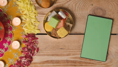 Overhead-Shot-Of-Indian-Sweets-In-Bowl-On-Table-Decorated-To-Celebrate-Festival-Of-Diwali-With-Digital-Tablet