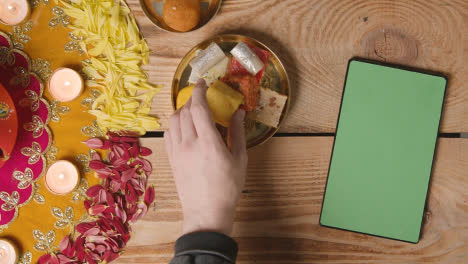 Overhead-Shot-Of-Indian-Sweets-In-Bowl-On-Table-Decorated-To-Celebrate-Festival-Of-Diwali-With-Digital-Tablet