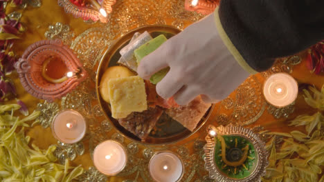 Fotografía-Cenital-De-La-Mano-Recogiendo-Dulces-Indios-En-Un-Tazón-Sobre-Una-Mesa-Decorada-Para-Celebrar-El-Festival-De-Diwali-1