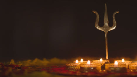 Metal-Trishula-Statue-Divine-Trident-Symbol-Of-Hinduism-On-Decorated-Table-With-Tea-Lights