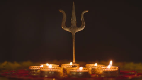 Metal-Trishula-Statue-Divine-Trident-Symbol-Of-Hinduism-On-Decorated-Table-With-Tea-Lights