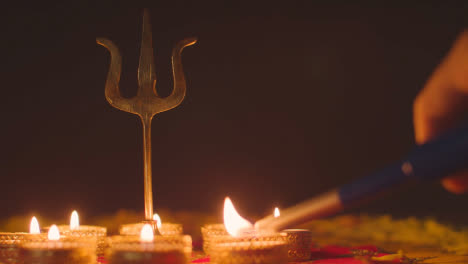 Iluminación-Manual-De-Velas-De-Té-Alrededor-De-La-Estatua-De-Trishula-De-Metal-Símbolo-Del-Tridente-Divino-Del-Hinduismo-En-Una-Mesa-Decorada