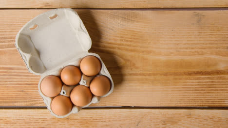 Fotografía-Cenital-De-Seis-Huevos-En-Una-Caja-De-Cartón-Que-Se-Abre-Sobre-Una-Mesa-De-Madera