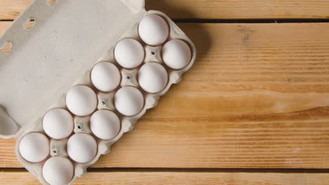 Fotografía-Cenital-De-Doce-Huevos-En-Una-Caja-De-Cartón-Que-Se-Abre-Sobre-Una-Mesa-De-Madera