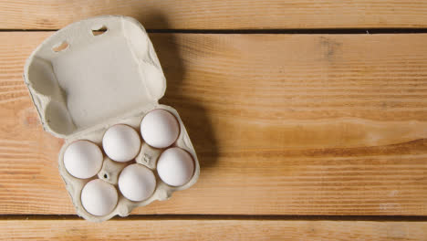 Überkopfaufnahme-Von-Sechs-Eiern-In-Kartons,-Die-Auf-Einem-Holztisch-Geöffnet-Werden