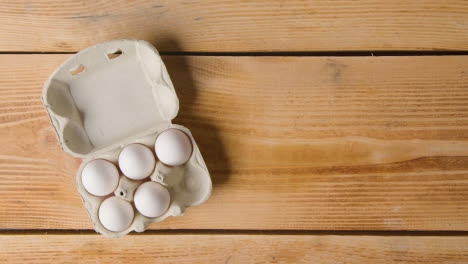 Overhead-Shot-Of-Hand-Taking-Out-Egg-From-Cardboard-Box-On-Wooden-Table