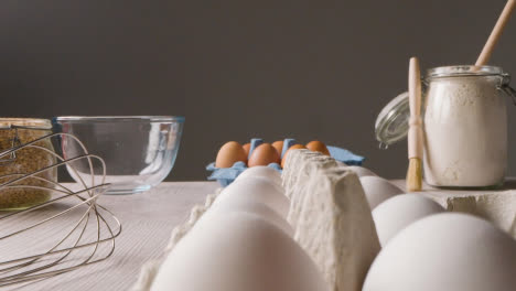 Foto-De-Estudio-De-Ingredientes-Para-Hornear-Y-Utensilios-En-La-Encimera-De-La-Cocina-Con-Una-Persona-Recogiendo-Huevo