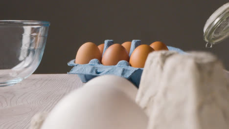 Foto-De-Estudio-De-Ingredientes-Para-Hornear-Y-Utensilios-En-La-Encimera-De-La-Cocina-Con-Una-Persona-Recogiendo-Huevos-1