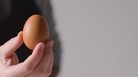 Close-Up-Studio-Shot-Of-Person-In-Apron-Holding-Up-Brown-Egg-To-Camera-1