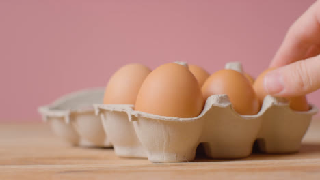 Studio-Shot-Of-Person-Opening-Cardboard-Box-Containing-Brown-Eggs-Against-Pink-Background-1
