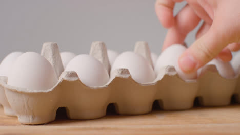 Studio-Shot-Of-Person-Opening-And-Choosing-From-Cardboard-Boxes-Containing-White-Eggs-Against-Grey-Background