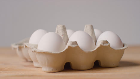 Studio-Shot-Of-Person-Opening-Cardboard-Box-Containing-Brown-Eggs-Against-Grey-Background