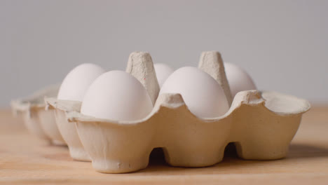 Studio-Shot-Of-Person-Opening-And-Choosing-From-Cardboard-Boxes-Containing-White-Eggs-Against-Grey-Background-1