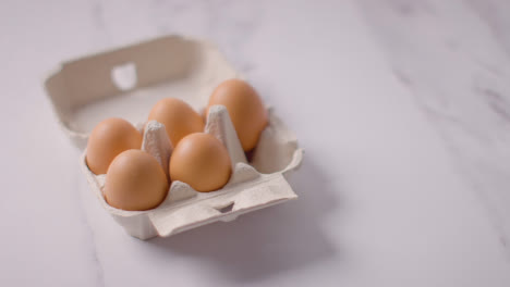 Person-Choosing-Egg-From-Open-Cardboard-Box-On-Marble-Work-Surface-Background