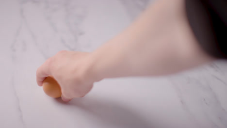 Studio-Shot-Of-Hand-Picking-Up-Single-Brown-Egg-On-Marble-Work-Surface-Background