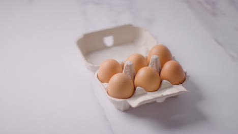 Person,-Die-Eine-Schachtel-Mit-Braunen-Eiern-Auf-Dem-Hintergrund-Der-Marmorarbeitsfläche-Aufhebt