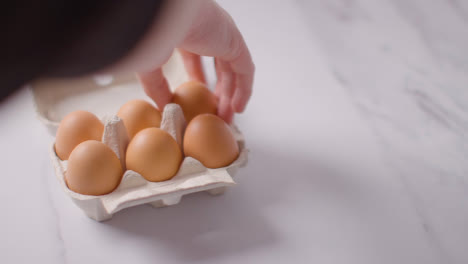 Person-Choosing-Egg-From-Open-Cardboard-Box-On-Marble-Work-Surface-Background-1