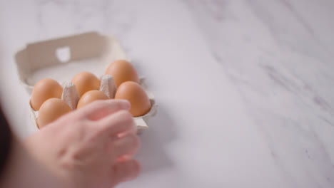 Person-Choosing-Egg-From-Open-Cardboard-Box-On-Marble-Work-Surface-Background-2