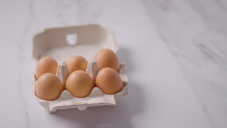 Person-Picking-Up-Box-Of-Brown-Eggs-On-Marble-Work-Surface-Background-2