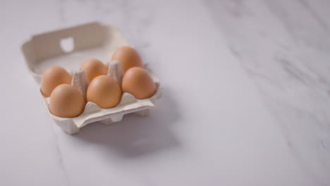 Person-Picking-Up-Box-Of-Brown-Eggs-On-Marble-Work-Surface-Background-3