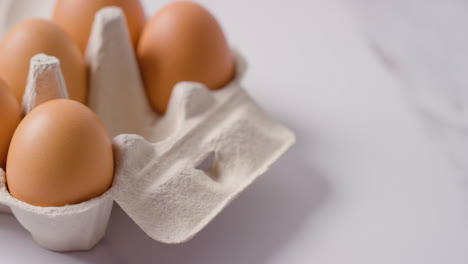 Person-Choosing-Egg-From-Open-Cardboard-Box-On-Marble-Work-Surface-Background-3