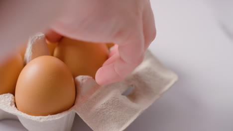 Studio-Shot-Of-Person-Choosing-Brown-Egg-From-Open-Cardboard-Box-On-Marble-Work-Surface-Background-3