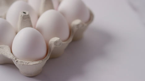 Studio-Shot-Of-Person-Choosing-White-Egg-Into-Open-Cardboard-Box-On-Marble-Work-Surface-Background