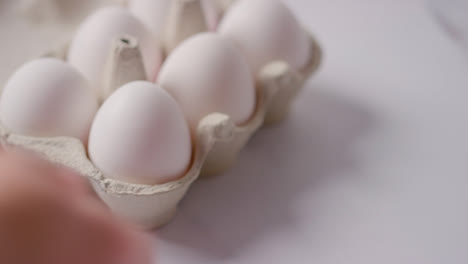 Studio-Shot-Of-Person-Choosing-White-Egg-Into-Open-Cardboard-Box-On-Marble-Work-Surface-Background-1