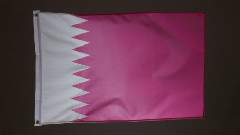 Studio-Shot-Of-Flag-Of-Qatar-Flying-Against-Black-Background